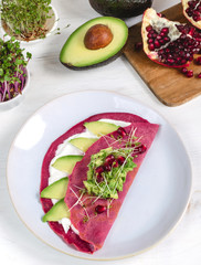 Tasty appetizing beetroot pancakes served on plate with avocado, sprouts and pink radish, white...