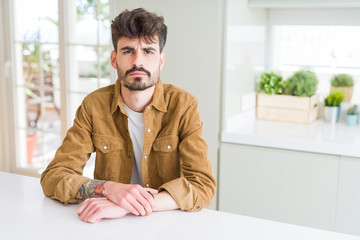 Young man wearing casual jacket sitting on white table skeptic and nervous, frowning upset because...