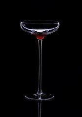 Beautiful empty cocktail glass on a high stem is isolated on a black background with reflection. Selective focus.