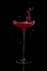 Colorful cocktail with splashes in a glass on a high thin leg is isolated on black with reflection.