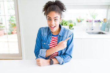 Beautiful young african american woman with afro hair wearing casual denim jacket cheerful with a smile of face pointing with hand and finger up to the side with happy and natural expression on face