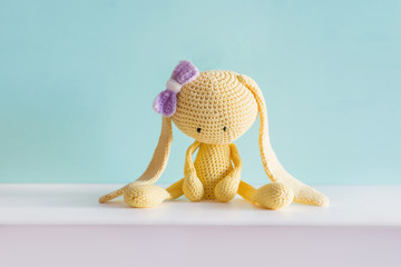 Soft toy knitted hare. Sitting yellow sad plush hare with a violet bow. Amigurumi.