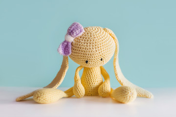 Soft toy knitted hare. Sitting yellow sad plush hare with a violet bow. Amigurumi.