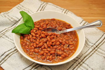 Baked Beans & Bacon Pieces Served in a White Bowl and Garnished with Fresh Basil