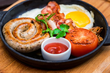 Nutritious meal with fried egg, sausage, bacon, tomato and sauce in frying pan