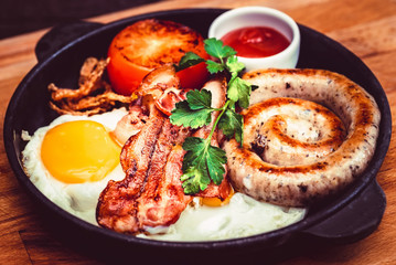 Nutritious meal with fried egg, sausage, bacon, tomato and sauce in frying pan