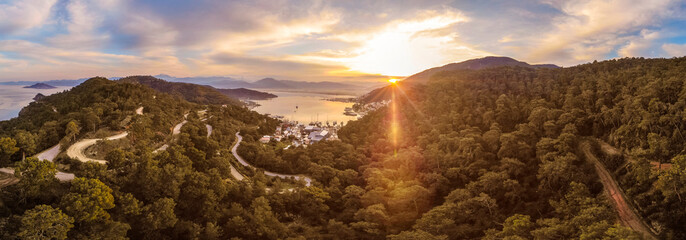 Sunrise over a mountainside covered in dense forest with a small harbour town at the bottom, Fethiye, Turkey panoramic