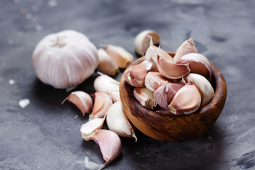 Garlic cloves and bulb in wooden bowl on dark background