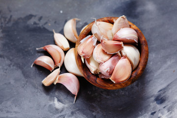 Garlic cloves and bulb in wooden bowl on dark background