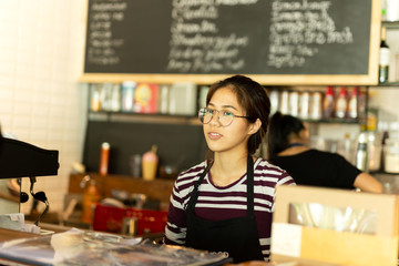 Asian girl with glasses waitress wearing apron standing in coffee shop.