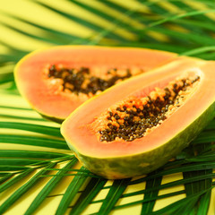 Exotic papaya fruit over tropical green palm leaves on yellow background. Copy space. Pop art design, creative summer concept. Raw vegan food.