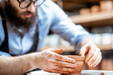 Handsome man as a potter worker in apron making clay jugs on the pottery wheel at the small manufacturing