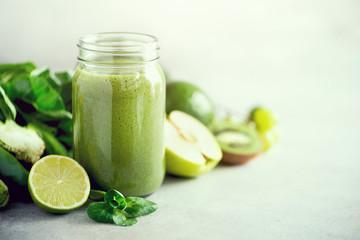 Glass jar mugs with green health smoothie, kale leaves, lime, apple, kiwi, grapes, banana, avocado, lettuce. Copy space, sunlight effect. Raw, vegan, vegetarian, detox, alkaline food concept.