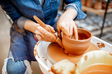 Woman making clay jug forming a shape with special tool on the pottery wheel, close-up view