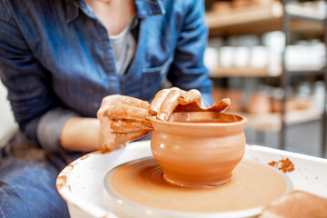 Woman making clay jug forming a shape with special tool on the pottery wheel, close-up view