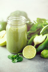 Glass jar mugs with green health smoothie, kale leaves, lime, apple, kiwi, grapes, banana, avocado, lettuce. Copy space, sunlight effect. Raw, vegan, vegetarian, detox, alkaline food concept.