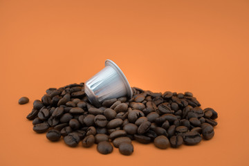 Espresso coffee capsule or coffee pod on coffee beans, orange background.