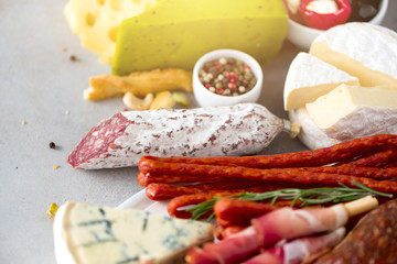 Traditional italian antipasto, cutting board with salami, cold smoked meat, prosciutto, ham, cheeses, olives, capers on grey background. Cheese and meat appetizer.