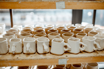 Clay cups and jugs on the shelves drying at the pottery
