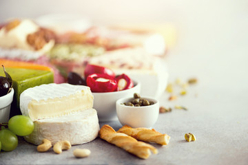 Assortment of hard, semi-soft and soft cheeses with olives, grissini bread sticks, capers, grape, on grey concrete backgound. Top view, copy space, flat lay. Cheese selection appetizer plate.