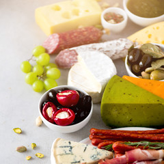 Traditional italian antipasto, cutting board with salami, cold smoked meat, prosciutto, ham, cheeses, olives, capers on grey background. Cheese and meat appetizer.