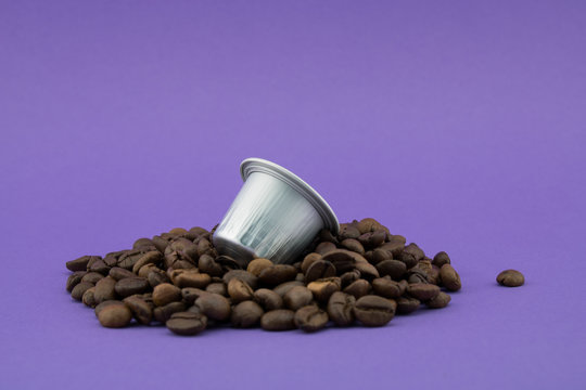 Espresso coffee capsule or coffee pod on coffee beans, purple background. Capsules.