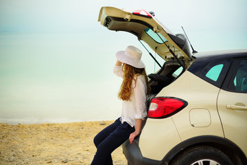 View of young woman traveler looking at sea sunset, sitting on hatchback car with the copy space.