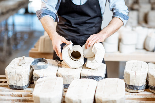 Male worker getting clay products from the gypsum forms at the pottery manufacturing, close-up view
