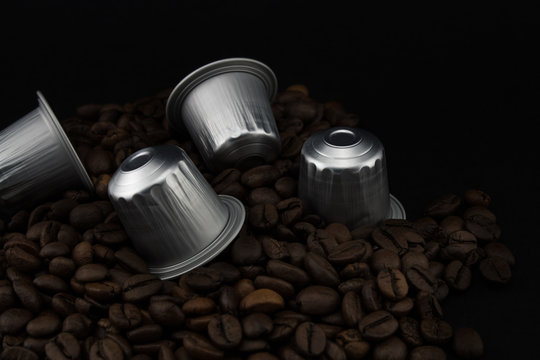 Espresso coffee capsules or coffee pods on coffee beans, black background.
