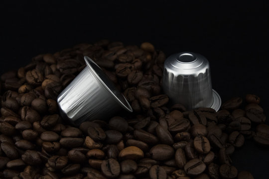 Espresso coffee capsules or coffee pods on coffee beans, black background.