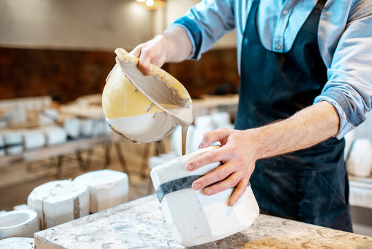 Worker pouring special liquid into the gypsum form making ceramic products at the pottery manufacturing, close-up view