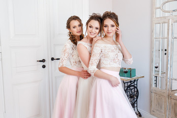 bride hugs with two bridesmaids in the morning in a bright room