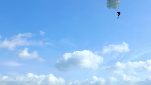 Unrecognizable skydiver with parachute flies against the blue sky with white clouds on summer day.