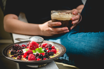 a young woman sits comfortably in an armchair in the morning sun, eats granola and drinks a coffee with whipped cream and cinnamon