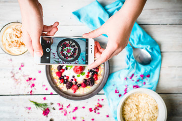 hands hold the phone, photographing colorful, healthy food on a light wooden table