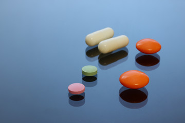 Bright colored tablets, pills, capsules on a glass table.
