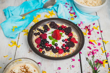 granola, fresh, nutritious breakfast with the addition of natural yoghurt, fresh and frozen fruit, and mint leaves,  on a white table decorated with spring flowers