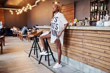 Beautiful african woman in stylish casual clothes posing near bar counter.