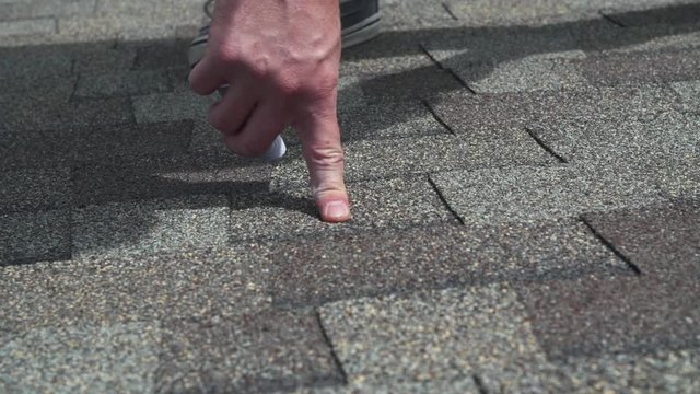 Insurance agent marking roof hail damage with chalk on shingles