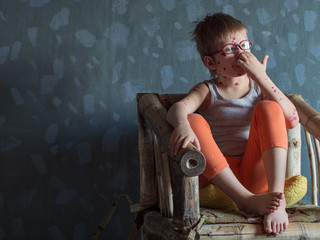 Upset blond child in pink glasses in straw chair has chicken pox. Mother smeared follicles with...