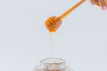 Honey dripping from wooden honey dipper on white background