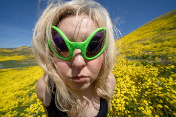 Spooky, creepy blonde woman wearing green alien sunglasses in a field of goldfield wildflowers in Carrizo Plain National Monument during the California superbloom