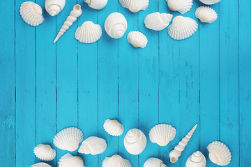 Fototapeta na wymiar White seashells on the sides of blue wooden background with empty space in the middle