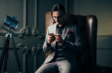 Young handsome man posing for a fashion shoot in a studio. Fashion as a lifestyle. Man wearing a beard. Model sitting on a sofa in tuxedo. Successful fashionable businessman. Business look advertising