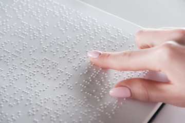 partial view of young woman reading braille text on white paper - obrazy, fototapety, plakaty