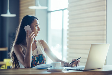 Beautiful girl working out a plan of the project and concept. Girl paints a website design on a laptop. student prints a message on the phone in the messenger. Development. Digital marketing