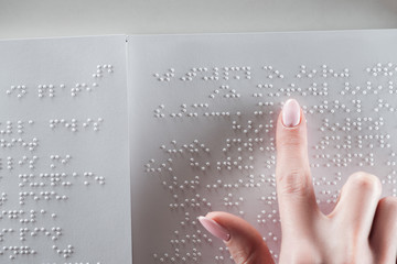 top view of young woman reading braille text on white paper