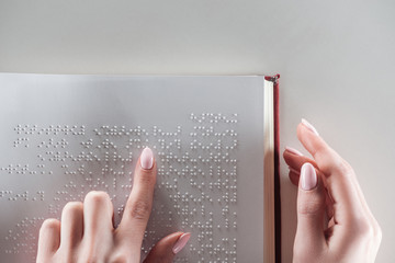 top view of young woman reading braille text on white paper - obrazy, fototapety, plakaty