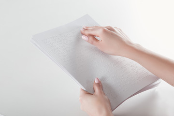 cropped view of young woman reading braille text with hand on white paper