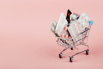 Shopping cart loaded with pills on a pink background. The concept of medicine and the sale of drugs. Copy space. © Plutmaverick